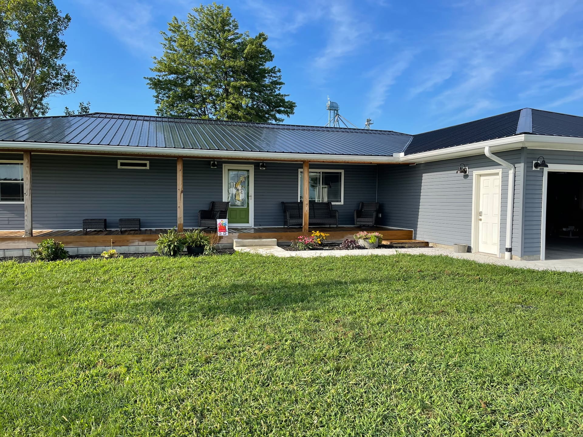 Single-story ranch home freshly painted slate gray with green front door and metal roof