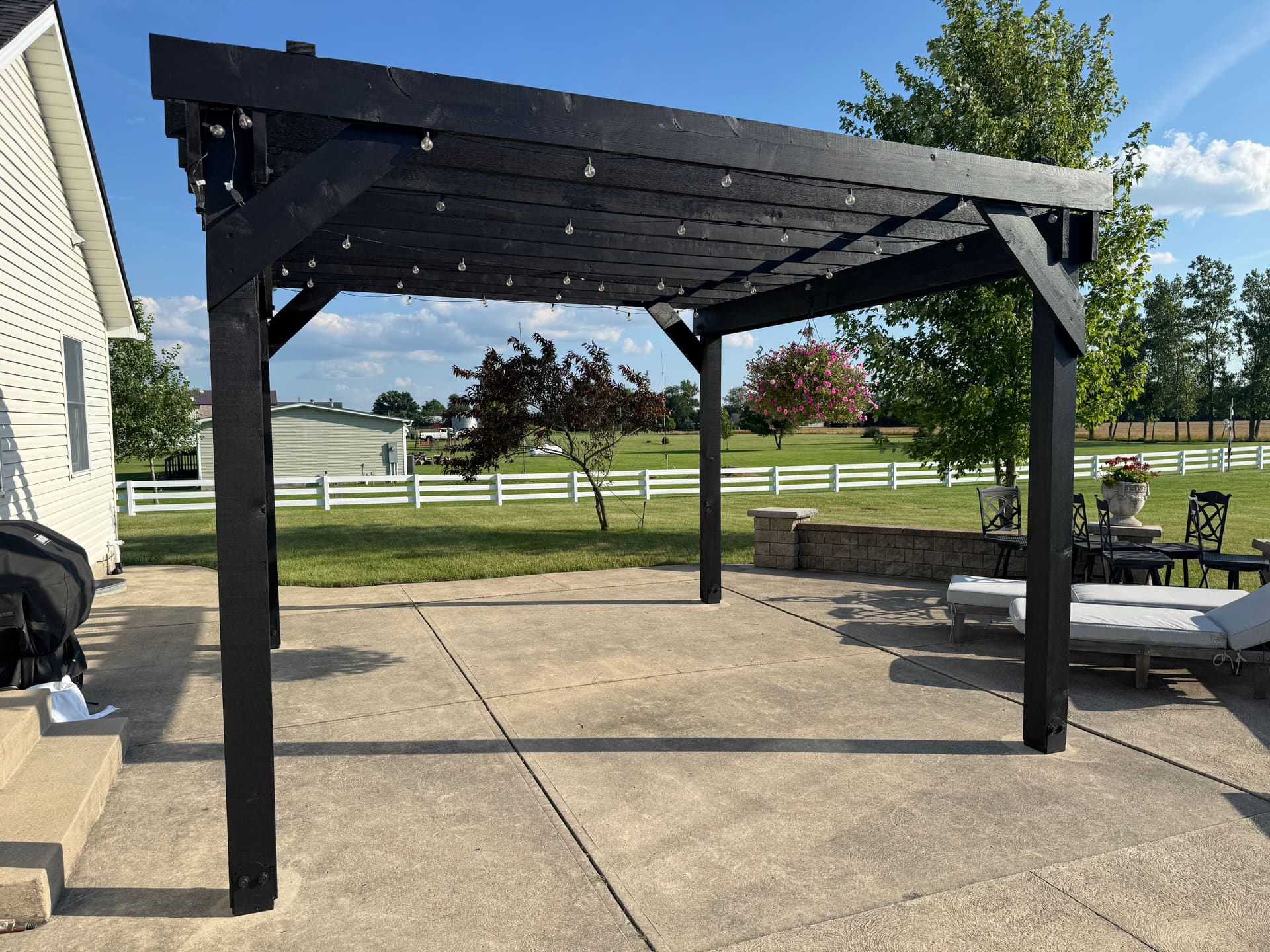 Side view of the black pergola with white fence backdrop